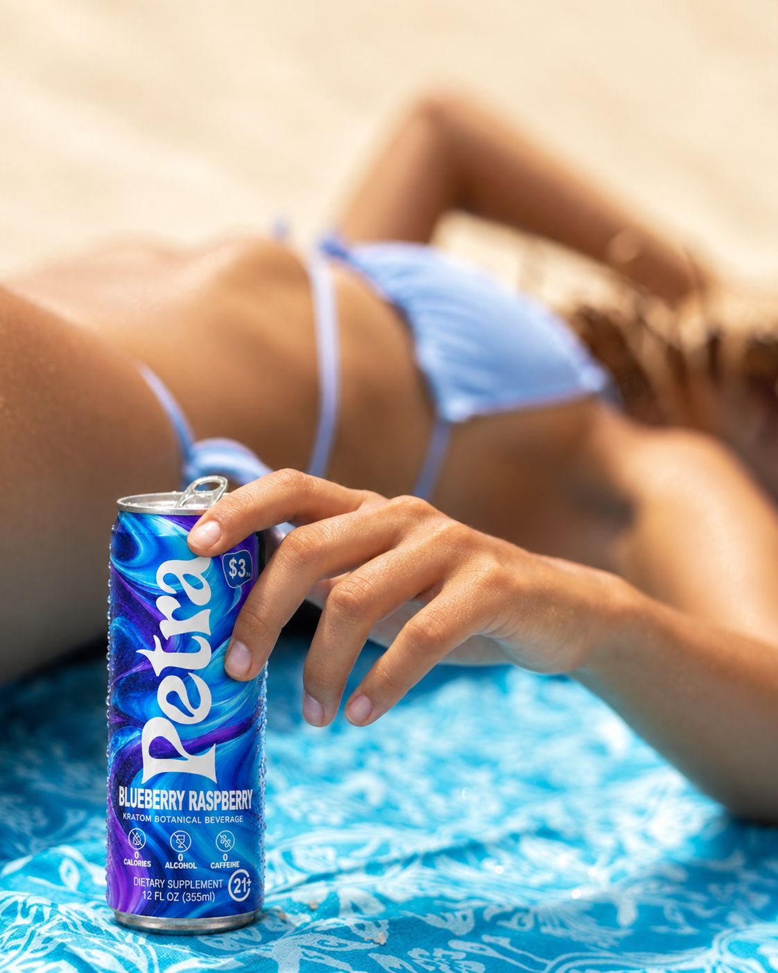 A Petra Blueberry Raspberry can resting on a beach towel in the sand